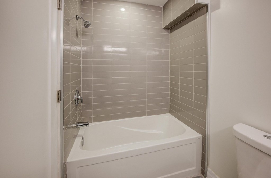A white bathtub with a shower head and a white toilet in a bathroom.