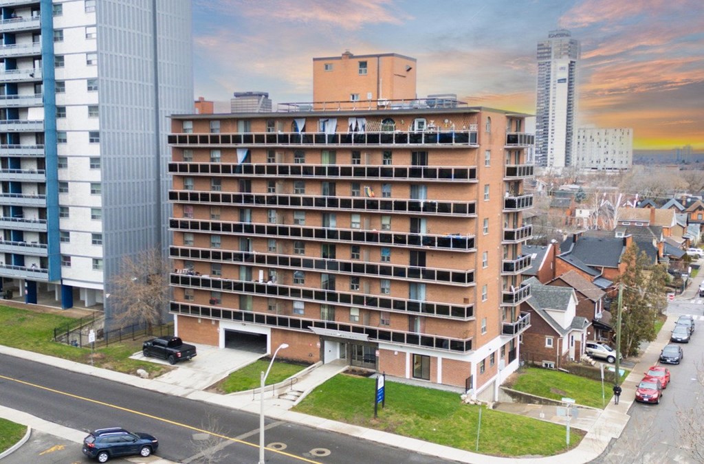 A large apartment building is situated on a street corner with cars parked along the curb.