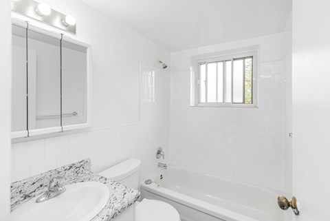 A white bathroom with a marble countertop and a window.