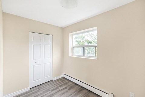 A room with a white door and a window with a view of trees outside.