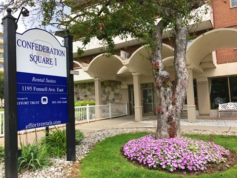 A sign for Confederation Square 1 rental suites stands in front of a building.