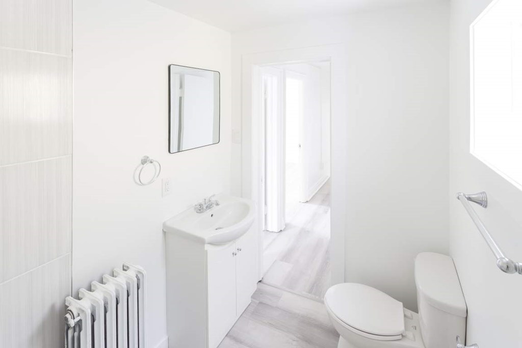 A white bathroom with a toilet, sink, and radiator.