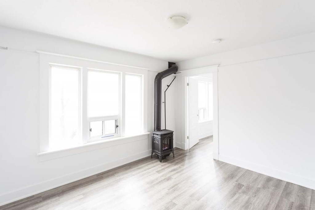 A wood stove is in a white room with a window.