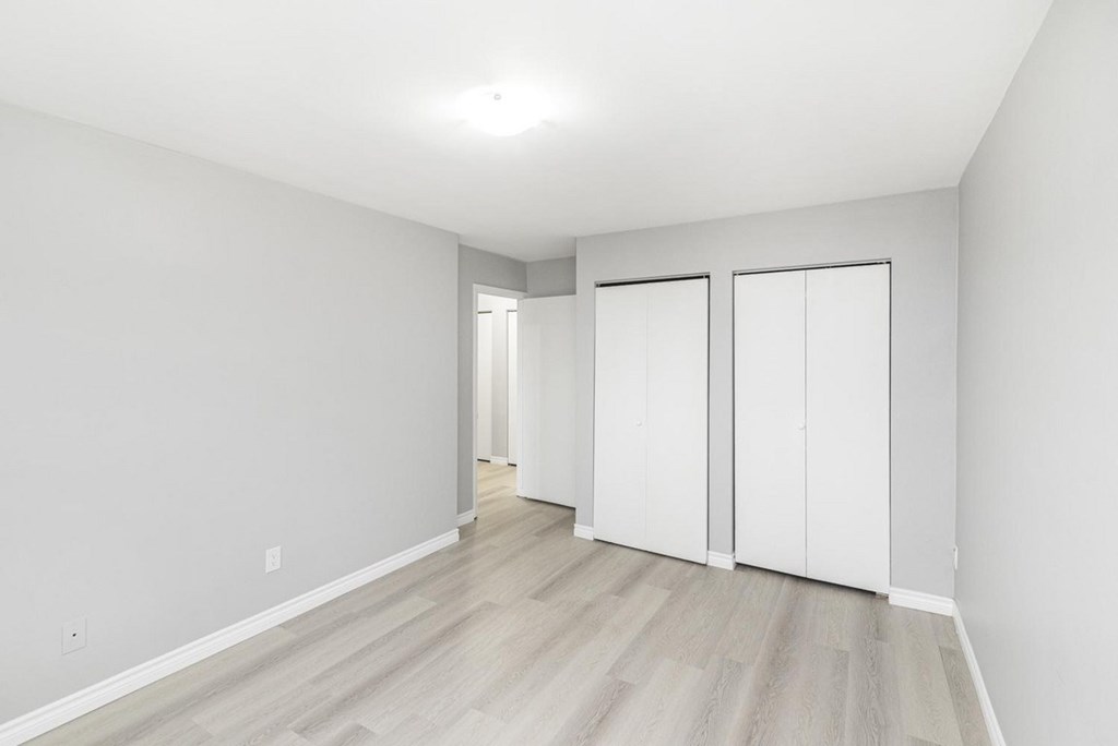 A room with white walls and a wooden floor with a white wardrobe.