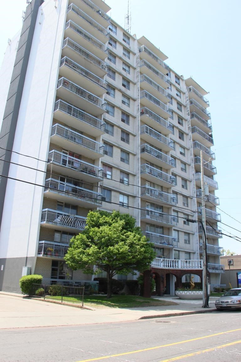 A tall apartment building with balconies and a tree in front.