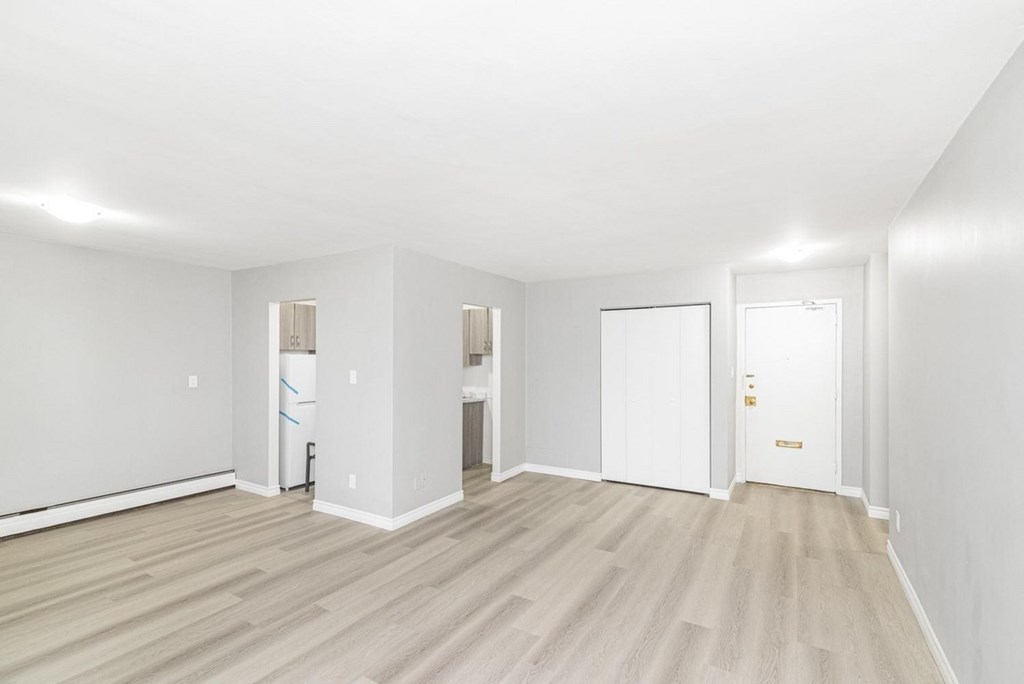 A room with white walls and wooden flooring with a door on the right.