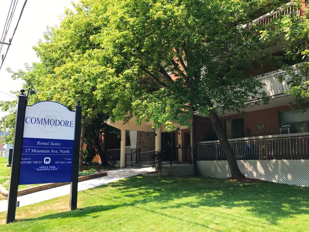 A sign for Commodore Apartment Homes stands in front of a building.