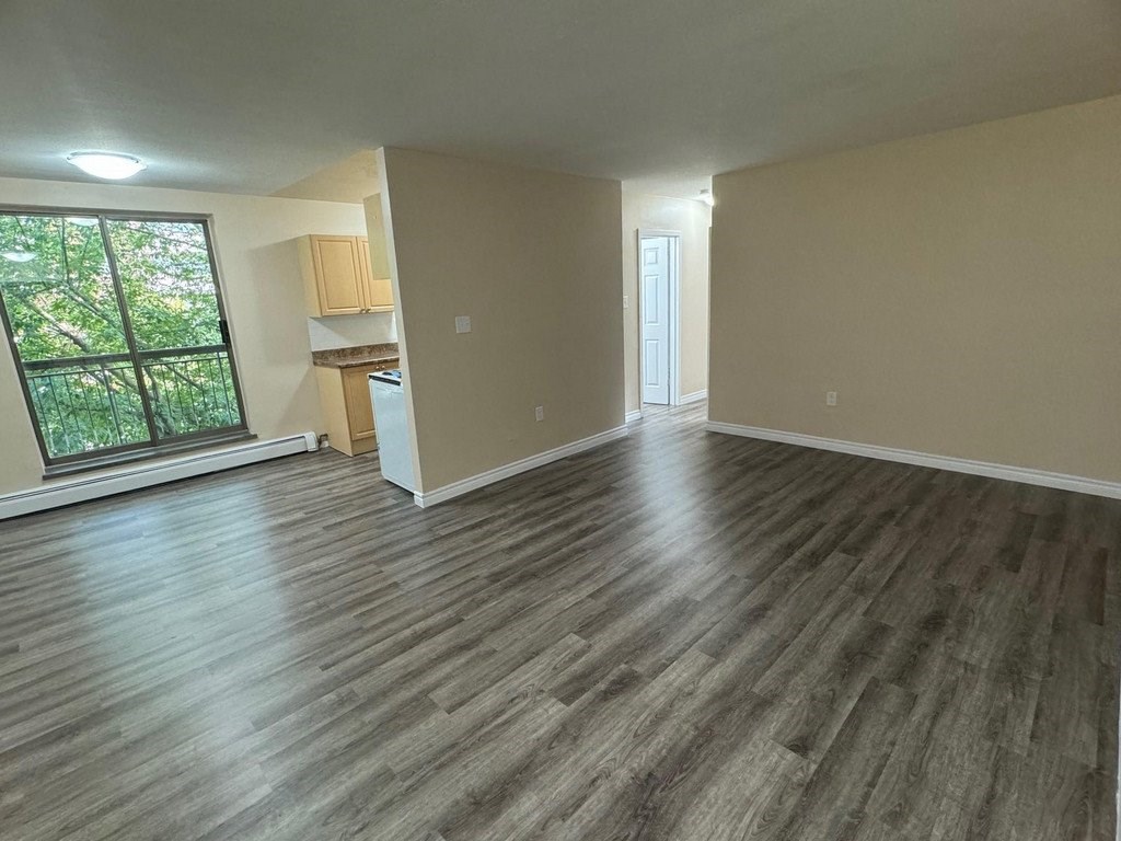 A room with wooden flooring and a window overlooking a tree-filled yard.