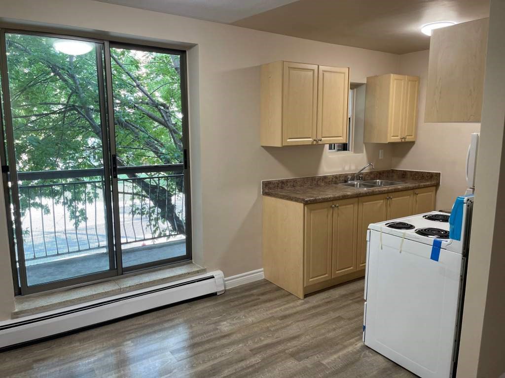 A kitchen with a white fridge, wooden cabinets, and a window with a view of trees.