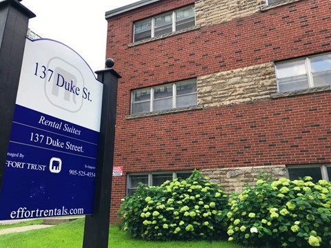 A sign for 137 Duke St. rental suites stands in front of a brick building.