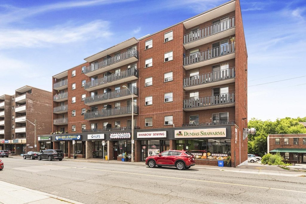 A red car is parked in front of a building with a sign that says "Dundas Shawarma.".