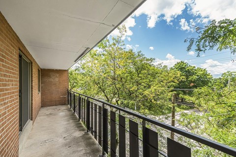 A balcony with a black railing and a view of trees and a blue sky.