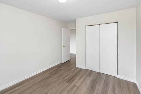 A room with white walls and wood flooring with a white closet.