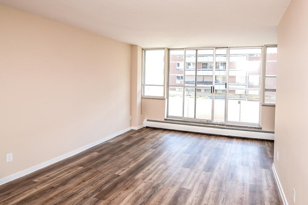 Empty room with wooden flooring and large windows.