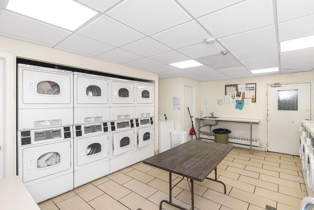 A laundry room with a row of washing machines and a table.