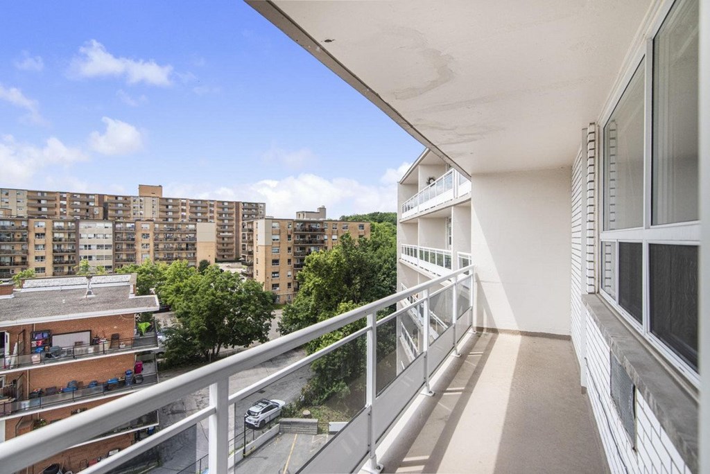 A balcony with a metal railing overlooks a parking lot and apartment buildings.