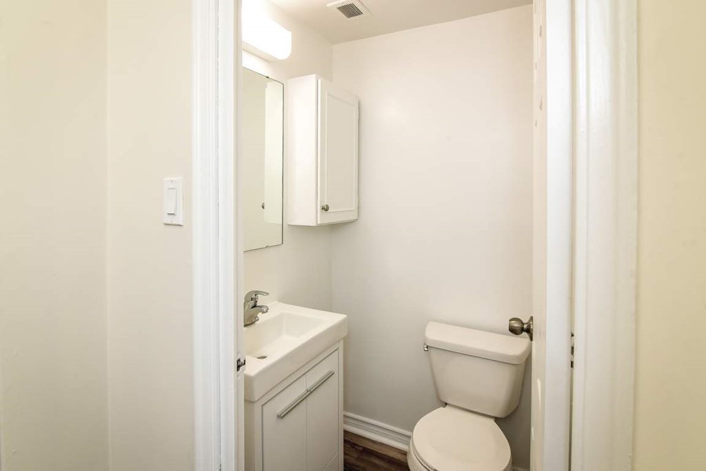 A white toilet is in a small bathroom with a sink and medicine cabinet.