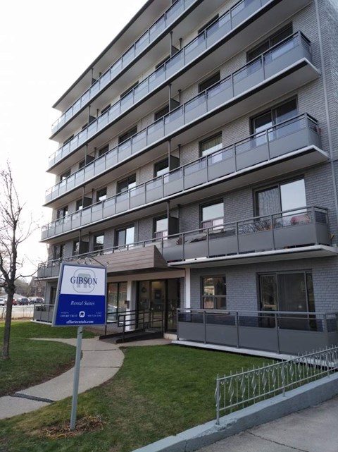 A Gibson apartment building with a blue sign in front.