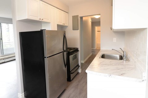 A black refrigerator is in a kitchen with white cabinets.