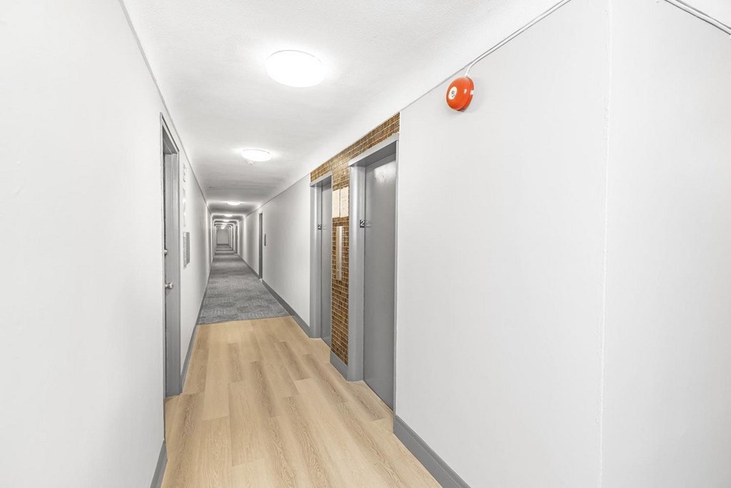 A long hallway with doors on both sides and a red object on the wall.