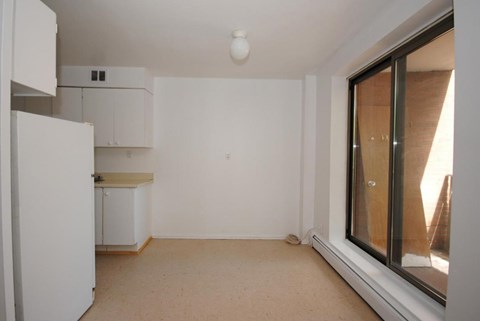 A white kitchen with a refrigerator, cabinets, and a window.