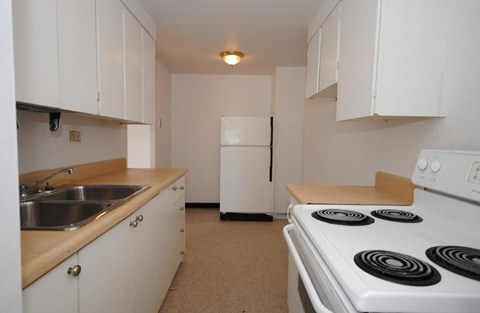 A white kitchen with a stove, sink, and refrigerator.