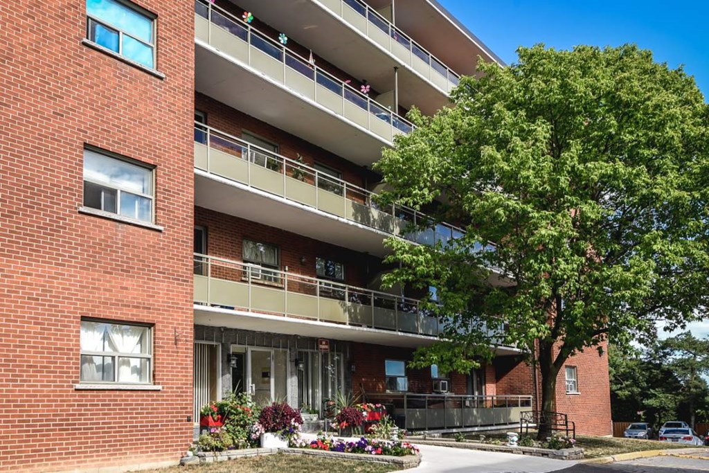 A red brick building with a balcony and a tree in front.
