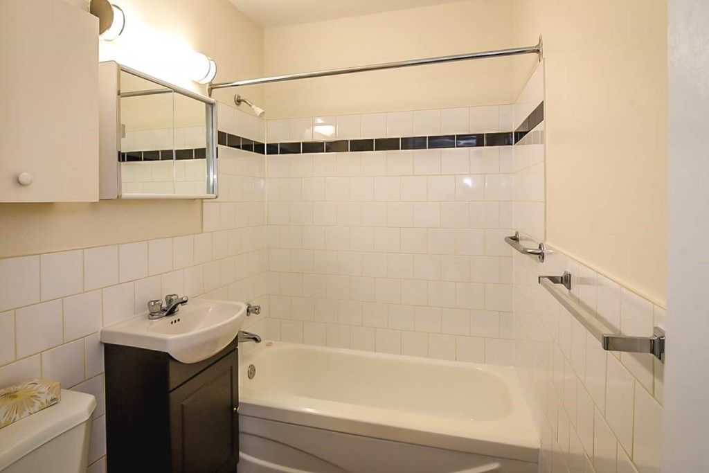 A white tiled bathroom with a white tub and a white toilet.