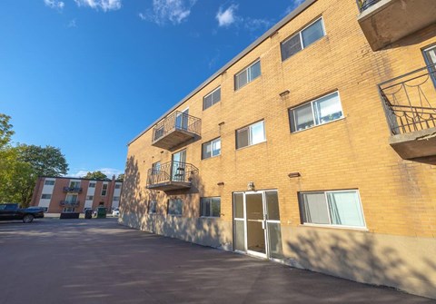 A sunny day at the parking lot of a brick apartment building.