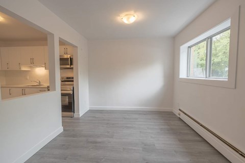 A spacious room with a window and a kitchen area in the background.