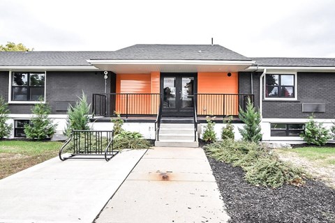 A grey house with an orange door and a black railing.