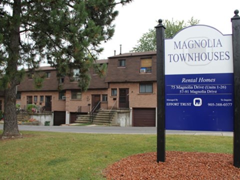 A sign for Magnolia Townhouses stands in front of a building.
