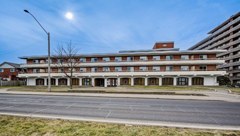 A large building with a red roof and white walls is surrounded by a grassy area and a street.