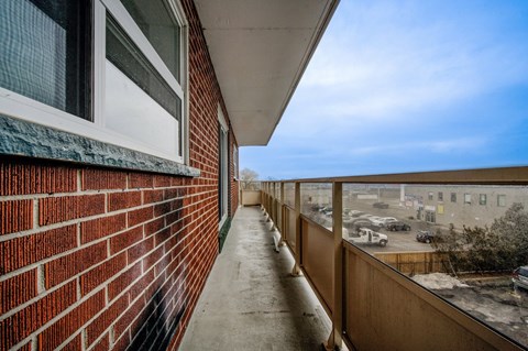 A balcony with a red brick wall and a view of a parking lot.