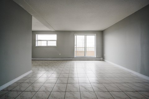 A large empty room with tiled floors and two windows.