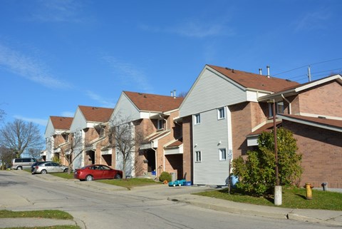 A row of houses with a red car parked in front of the first house.