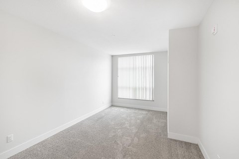 A room with a carpeted floor and a window with blinds.