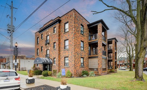 A red brick building with a black awning and a tree in front.