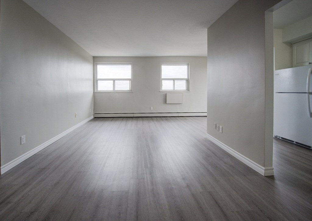 A spacious room with wooden floors and two windows.