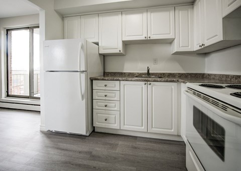 A white refrigerator stands in a kitchen with white cabinets and a marble countertop.