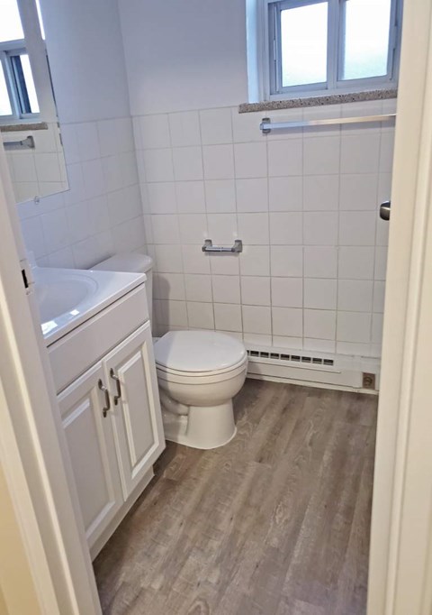 A white toilet in a small bathroom with a wooden floor.