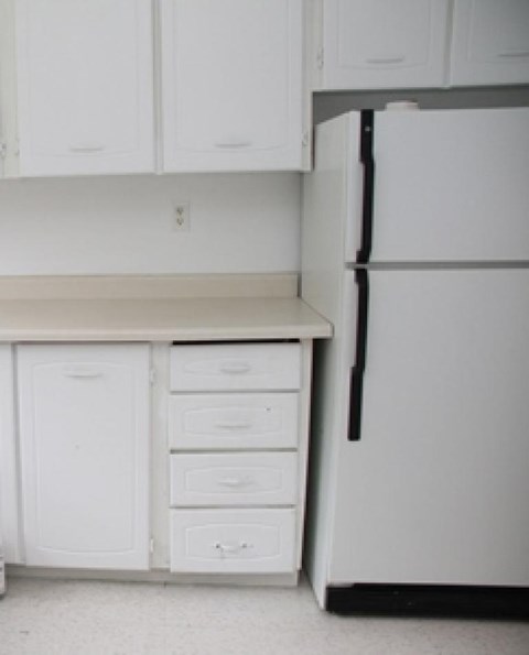 A white fridge in a kitchen with white cupboards.