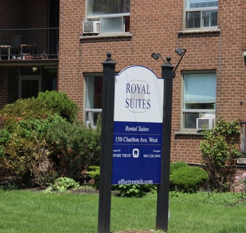 A sign for Royal Suites rental suites stands in front of a brick building.