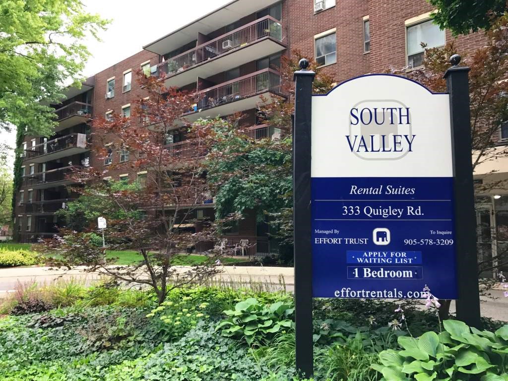 A sign for South Valley Apartments stands in front of a brick building.