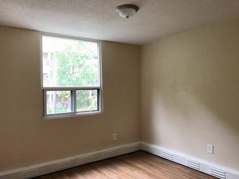 A room with a window and a smoke detector on the ceiling.
