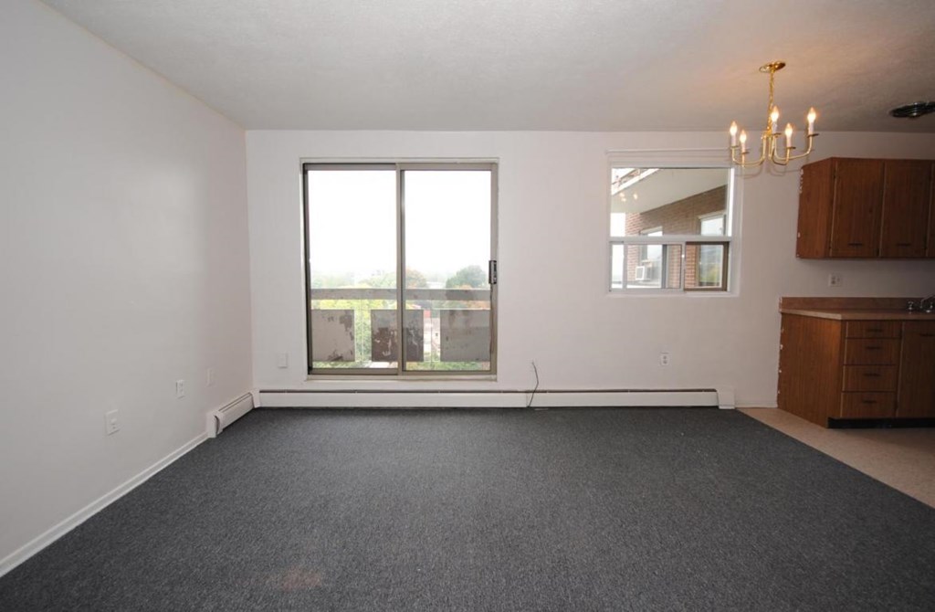 A large empty room with a grey carpet and a chandelier.