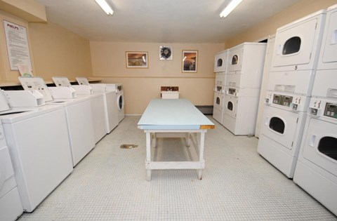 A laundromat with a row of washers and dryers on the left and a table in the middle.