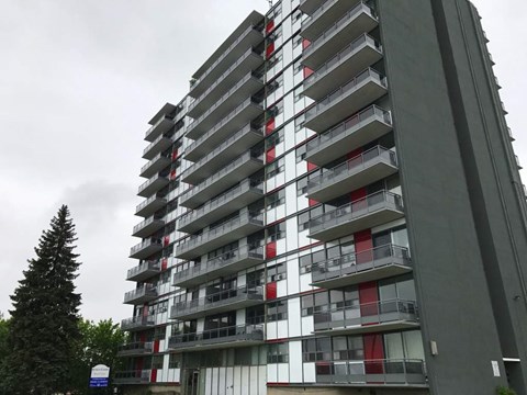 A tall building with balconies and a cloudy sky in the background.