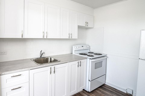 A white kitchen with a stove, sink, and cabinets.