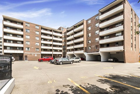 A parking lot in front of a multi-story apartment building with cars parked.